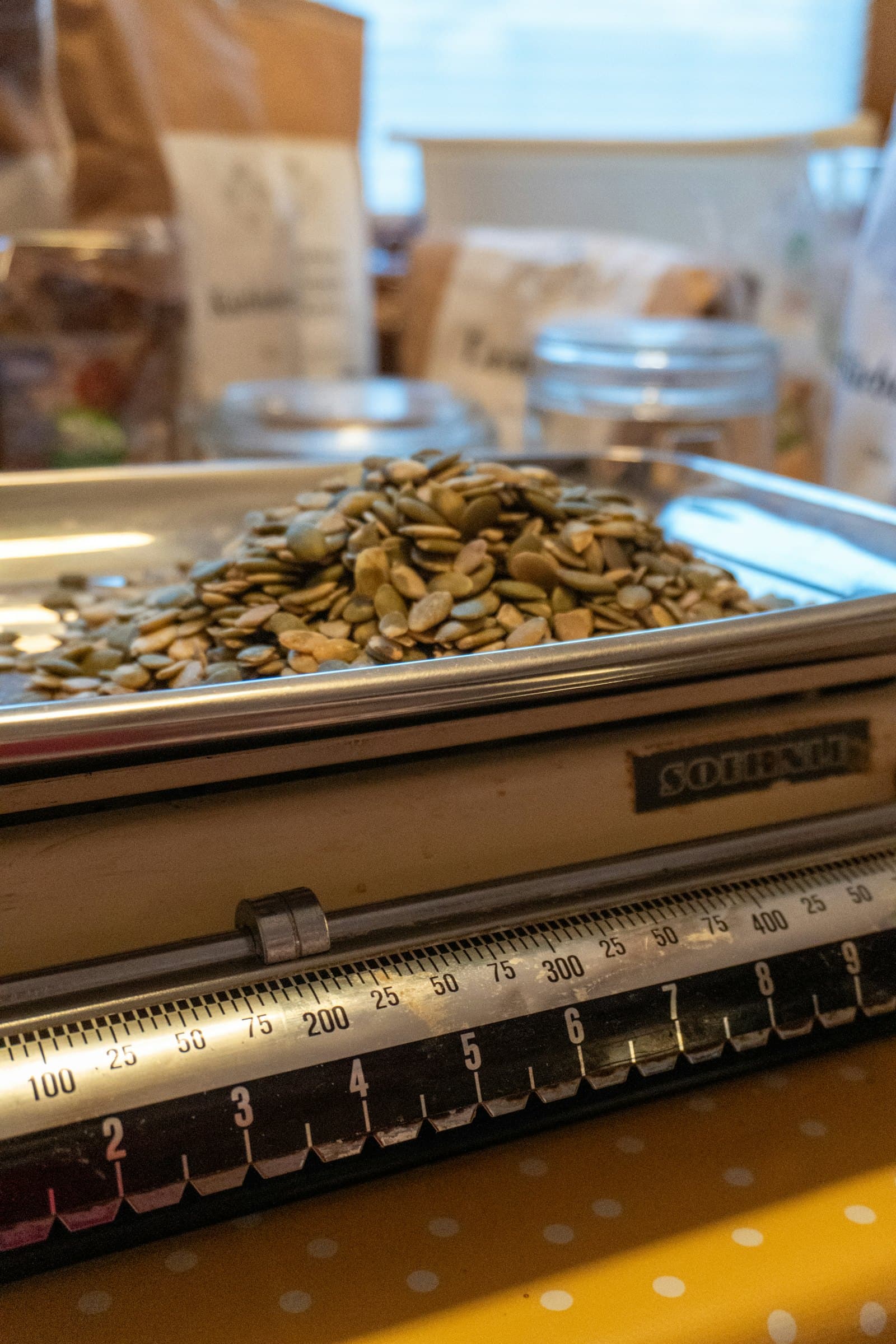 Seeds heaped on the pan of an old kitchen scale, its dial marked in grams