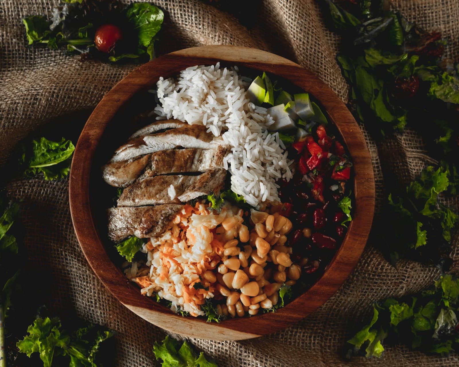 A wooden bowl of sliced chicken, rice and beans