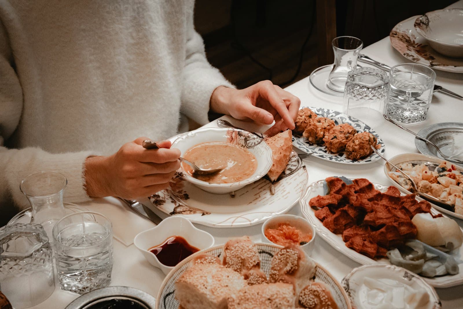 Someone eating a bowl of soup at a table laid with shared dishes
