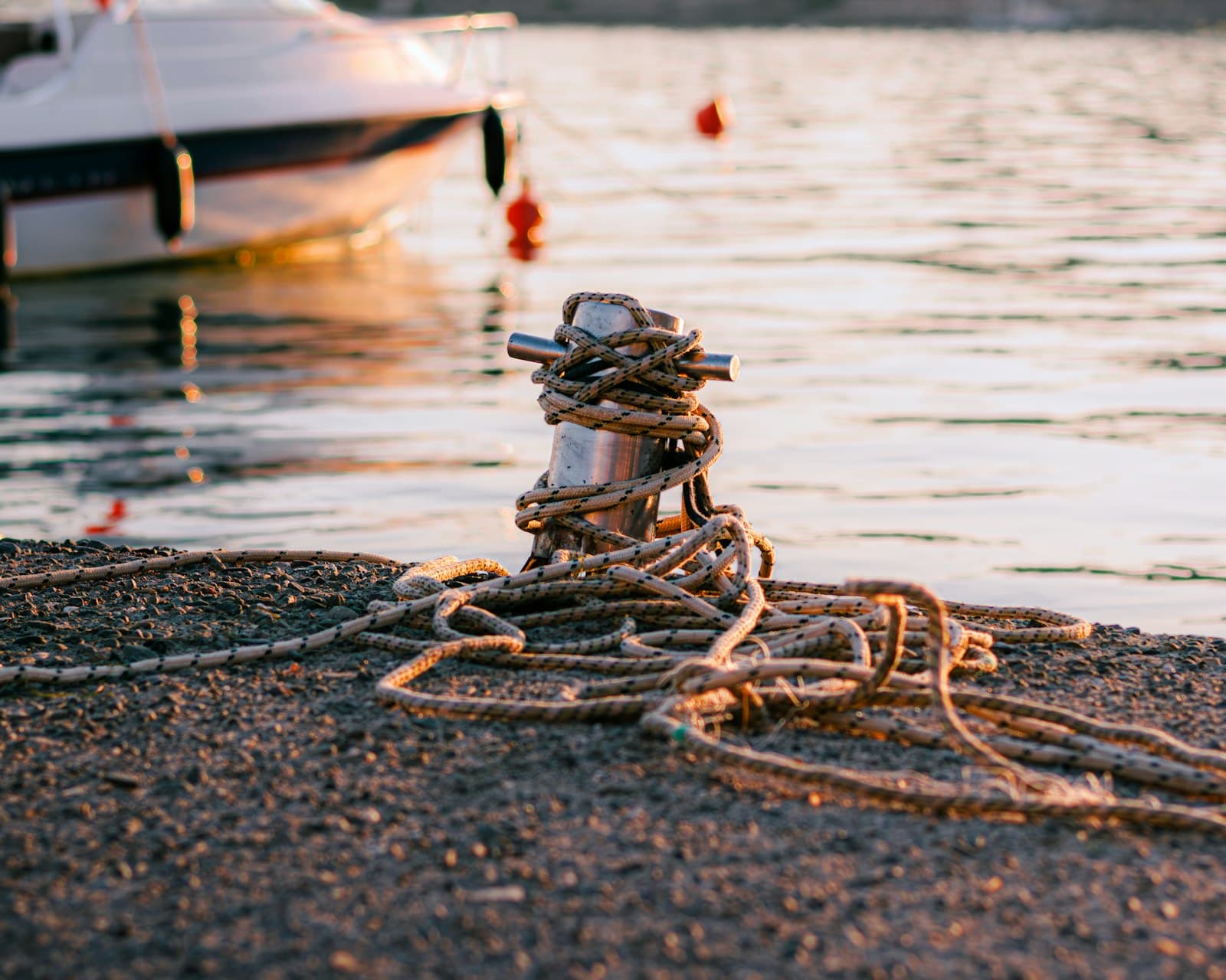 A mooring rope coiled around a cleat at the water's edge at sunset
