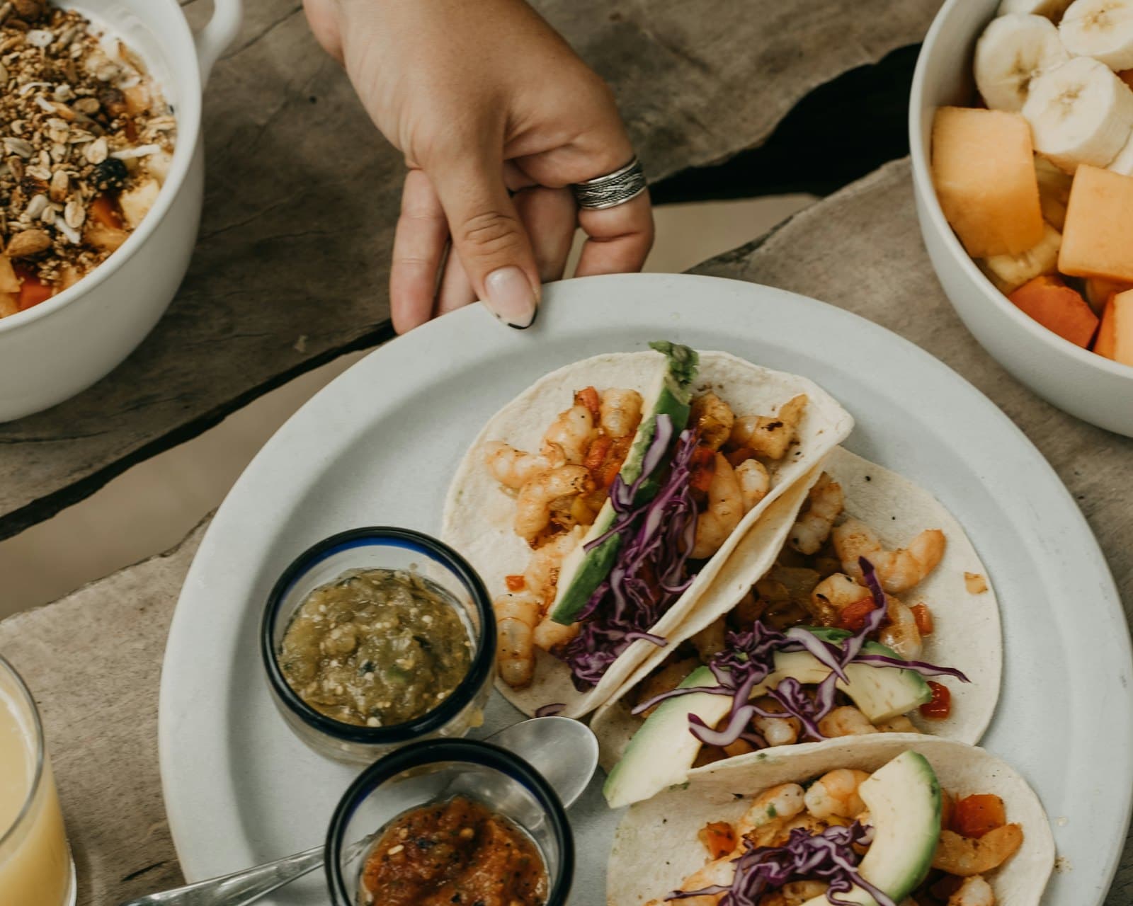 A hand setting down a plate of tacos on a weathered wooden table