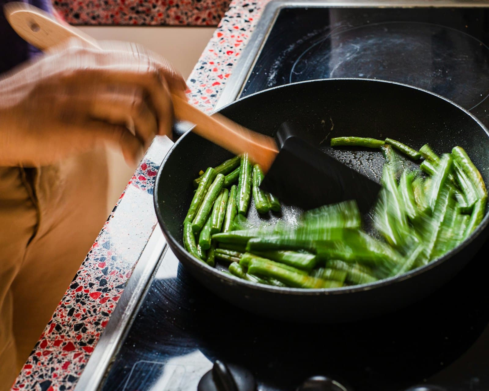 Someone turning green beans in a pan on the hob