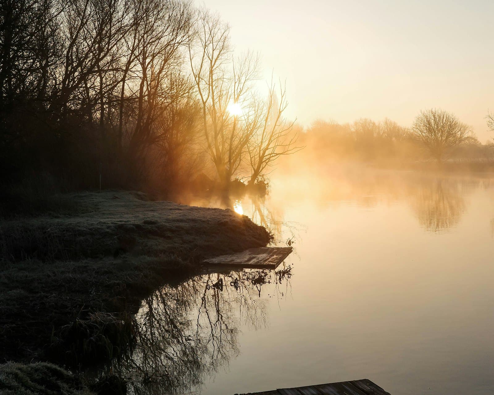 A completely still lake under morning mist at sunrise