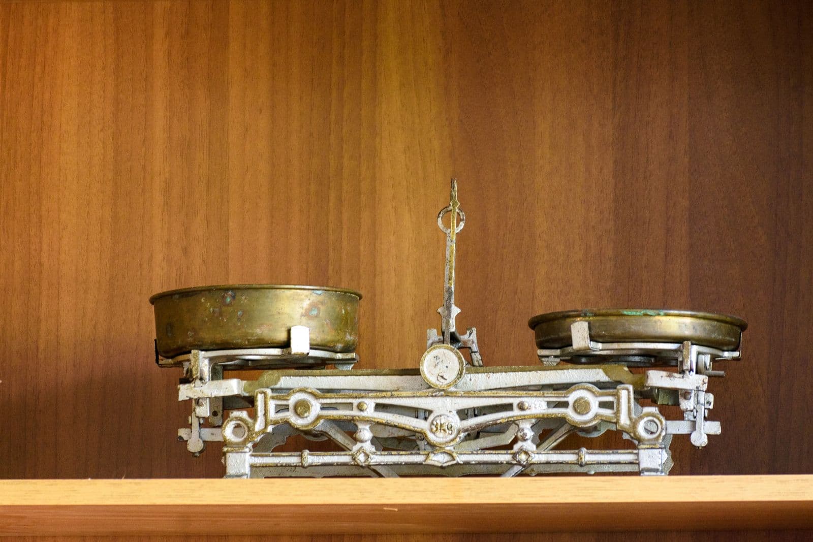 An old two-pan balance scale on a wooden shelf, its pans not quite level